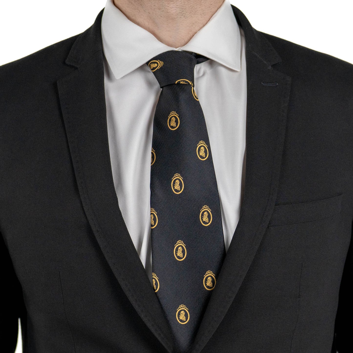 A close-up of a person wearing a black suit jacket and white dress shirt, with a black tie featuring small gold crest motifs.