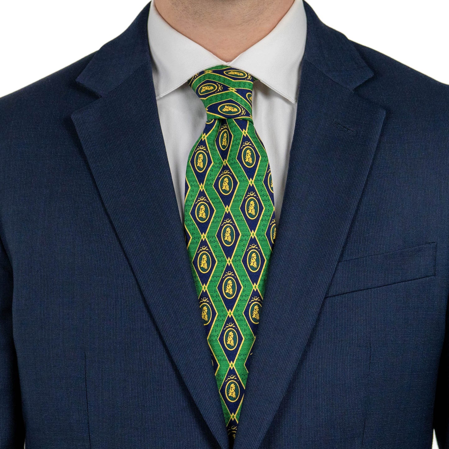 A close-up of a person wearing a navy suit jacket and white dress shirt, with a green tie featuring a repeating diamond pattern in blue and yellow with small crest motifs.