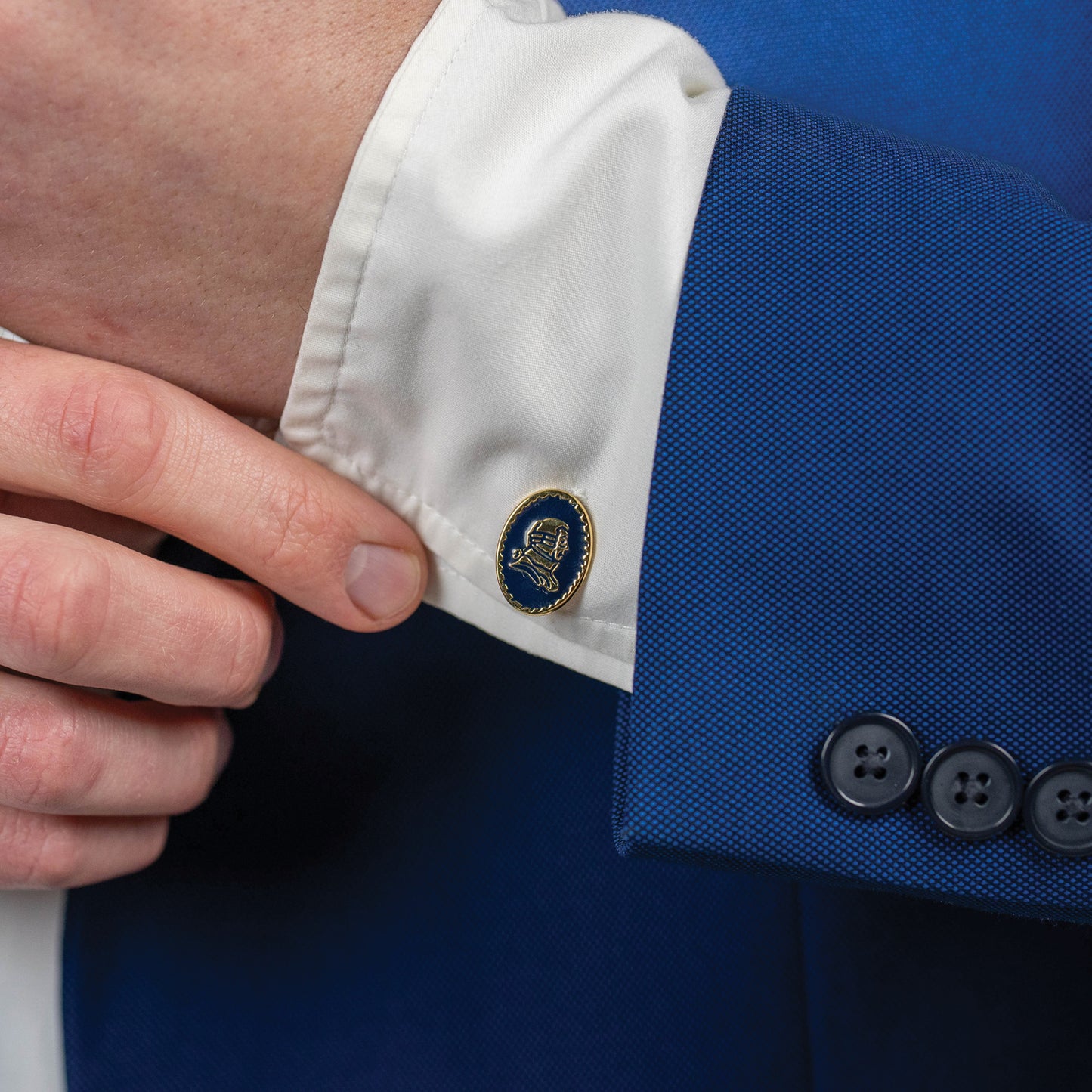 Close-up of a blue suit jacket with a lapel pin and white shirt cuff.
