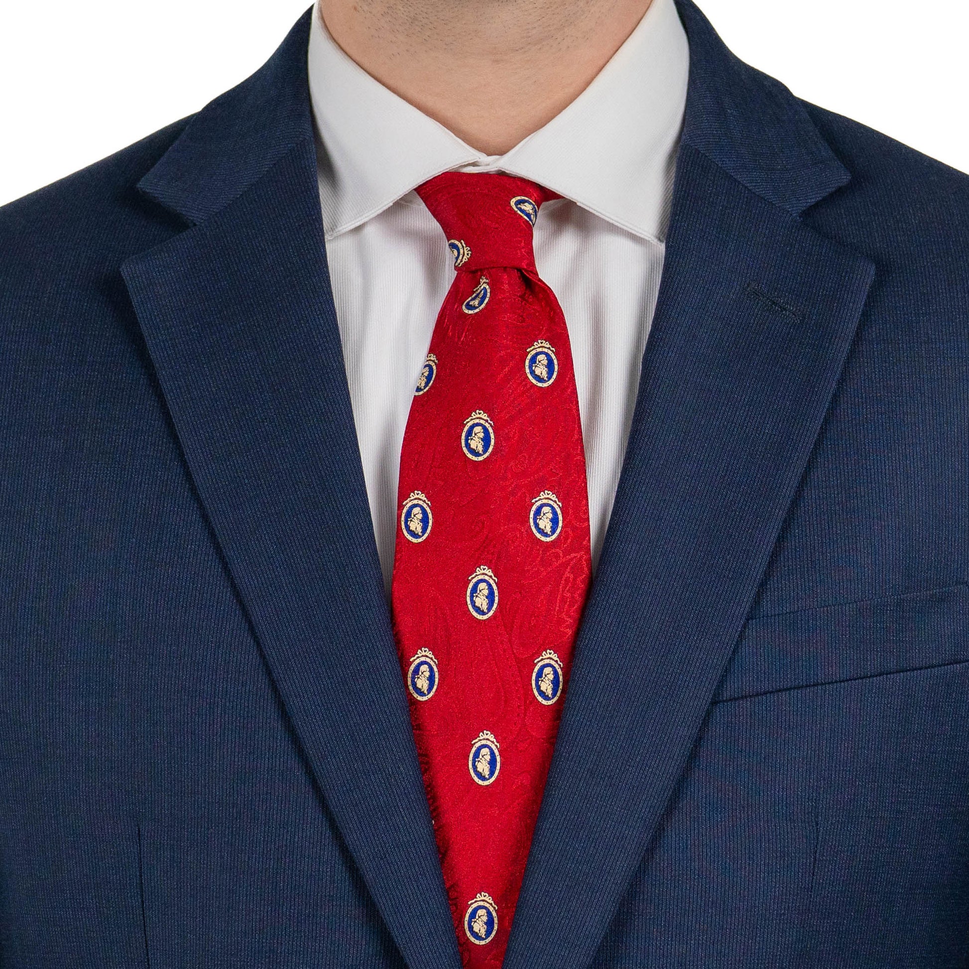 A close-up of a person wearing a navy suit jacket and white dress shirt, with a red tie featuring a subtle pattern and small blue-and-gold medallion motifs.